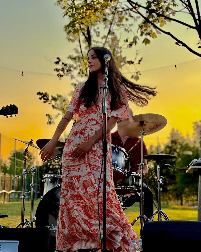 Giulia Gerardi al microfono, abito corallo, controluce al tramonto